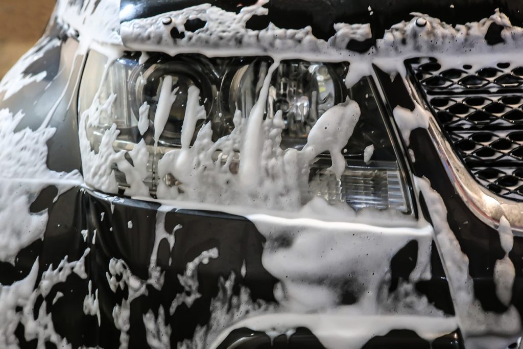 Car wash with soapy foam pouring over a car bumper.