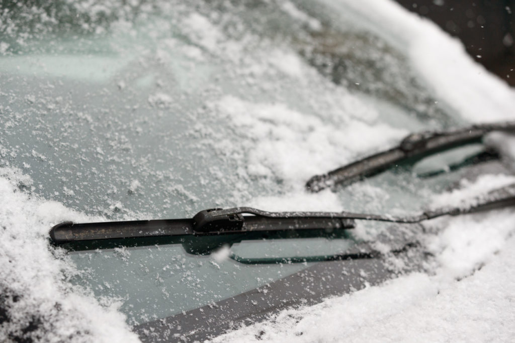 Car wiper blades clean snow from car windows. Flakes of snow covered the car with a thick layer. Safe driving with working wipers and clean windshield.