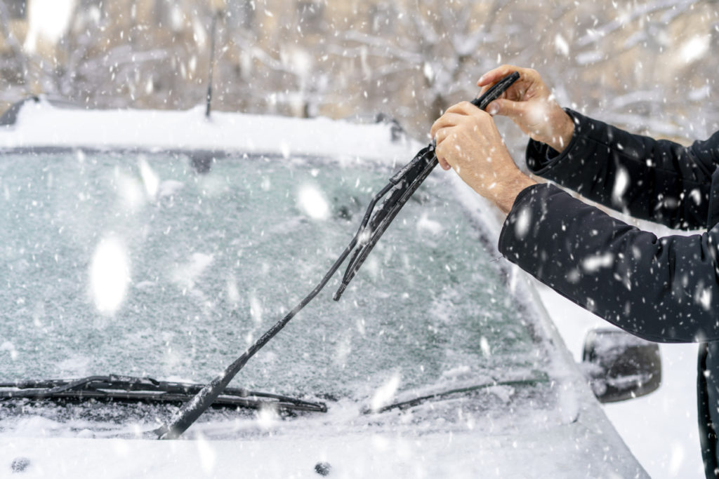 man adjusting and cleaning wipers of car in snowy weather