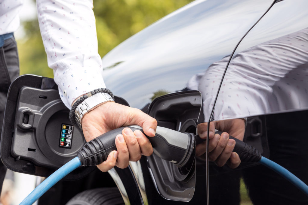 Human hand is holding charging connect power supply plugged into an electric car
