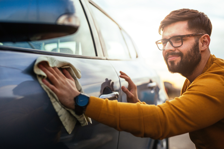 Photo of a satisfied young man polishing his car with microfiber cloth.