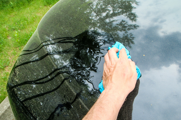 The spring detail of a car dirty from pollen. The hand is cleaning it with a wet rag.