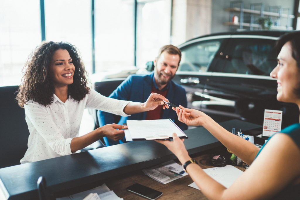 three people at dealership counter signing documents