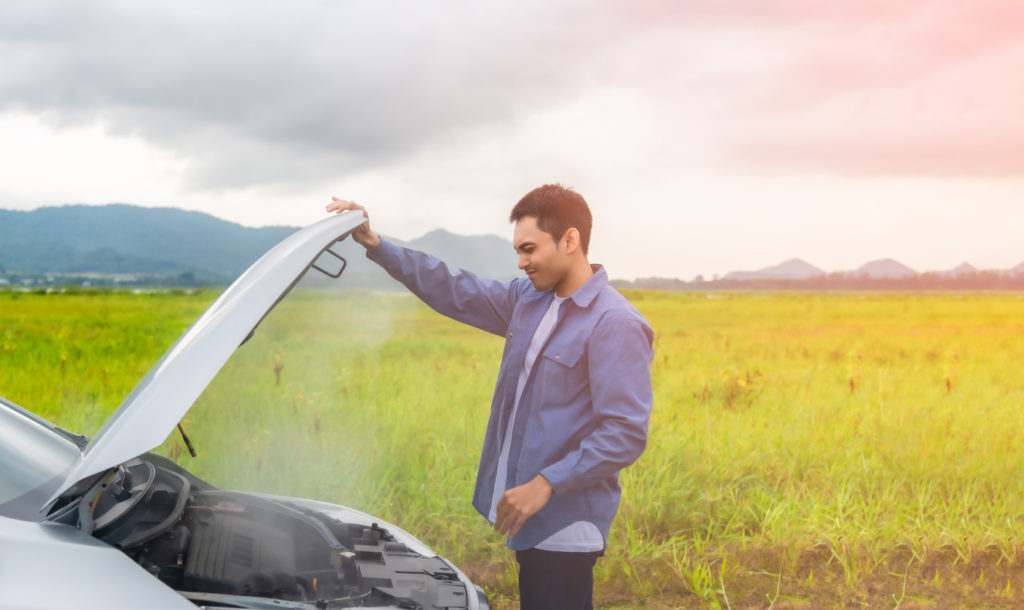 person looking under hood of car with steam rising from engine