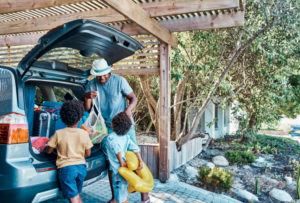 Excited black family packing their car trunk for a trip to the beach. Happy single dad and playful kids loading their boot for a summer vacation. Time to travel and have fun on a road trip together