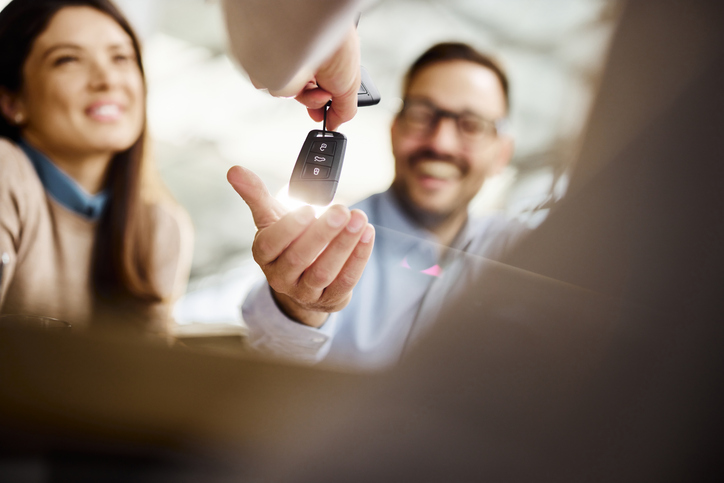 Close up of a couple receiving keys from a salesperson after buying a new car in a showroom. Copy space.